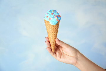 Female hand holding ice-cream cone on light background