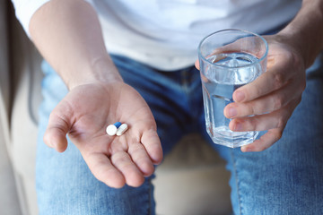 Young man with pills and glass of water at home, closeup