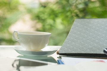 White coffee cup on a glass table with document on the side.