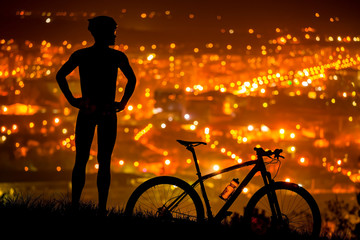 Obraz premium athlete is standing with bicycle, resting with the night city view
