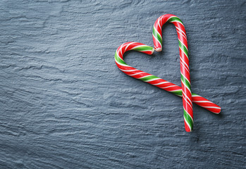 Heart shape made with Christmas candy canes on gray background