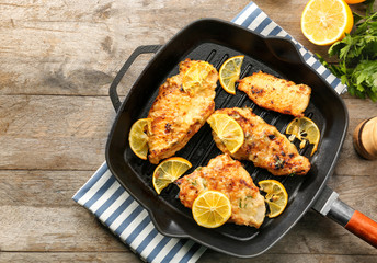Frying pan with tasty chicken piccata on wooden table