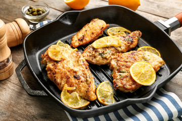 Frying pan with tasty Italian chicken piccata on table