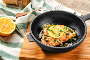 Frying pan with delicious chicken piccata on wooden board