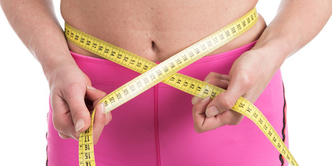 Close up of female hands measuring waist with measuring yellow tape. Fit and healthy woman on white background