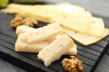 Composition of sliced cheese and walnut on black wooden board