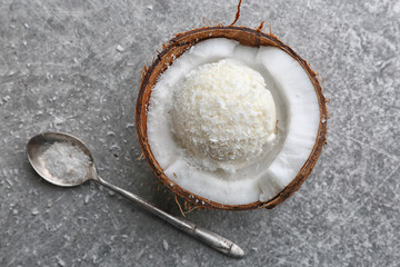 Fresh ball of ice cream in half of coconut and spoon on grey background