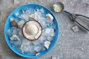 Half of coconut with fresh ice cream ball cooling on icy cubes in blue bowl