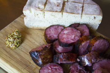 Portuguese rosted chorizo served with bread and mustard sauce in a wooden board 