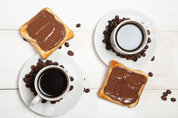 Two cups of coffee and toast with chocolate on a white wooden table