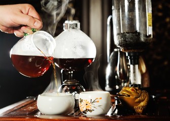 A man's hand pours black tea into a beautiful Chinese bowl on the background of a tea table. tea ceremony