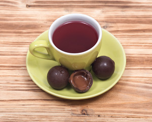 Wild berry tea in green cup with chocolate truffles on wooden vintage background
