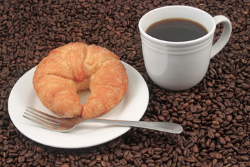 A white coffee cup with a pastry on a plat with fork on a background of coffee beans