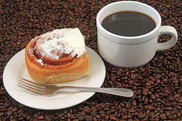 A white coffee cup with a pastry on a plat with fork on a background of coffee beans