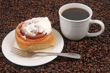A white coffee cup with a pastry on a plat with fork on a background of coffee beans