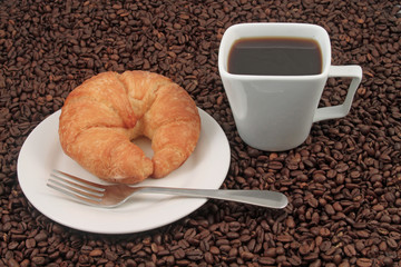 A white coffee cup with a pastry on a plat with fork on a background of coffee beans