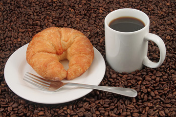 A white coffee cup with a pastry on a plat with fork on a background of coffee beans