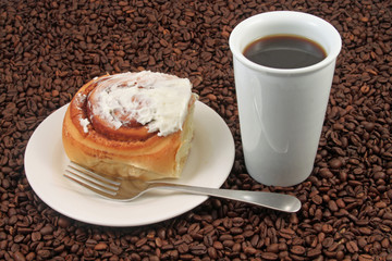 A white coffee cup with a pastry on a plat with fork on a background of coffee beans