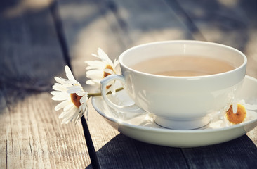 White cup and camomiles on a wooden table.