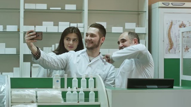 Cheerful team of pharmacist and interns take selfie via smartphone at workplace