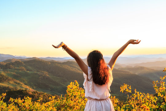 Asian teenage girl Asia ethnic cheerful front is a flower and overlooks the mountain complex and sky at sunset or sunrise on the mountain with copy space.