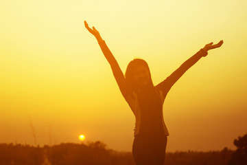 Fototapeta na wymiar Happy woman raised hands up on the sky at sunset