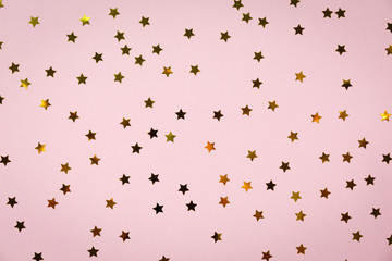Golden star sprinkles on pink. Festive holiday background. Celebration concept