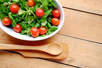 Cherry tomatoes and basil salad in a white cup on a wooden table.