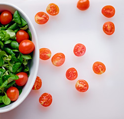 Cutted cherry tomatoes and basil salad on a white plate.