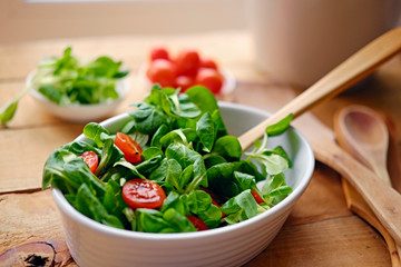 Cherry tomatoes and basil salad on a plate with a pot on a wooden table.