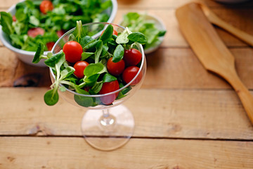 Cherry tomatoes and basil salad on a plate with a pot on a wooden table.