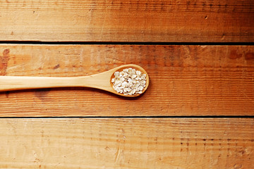 Wooden spoon with oat flakes over wooden pattern background.