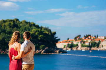 Fototapeta na wymiar A young couple hugs and looks at the island of Sveti Stefan in Montenegro.