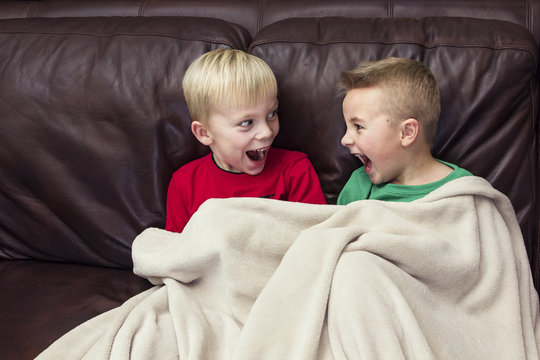 Two excited and happy boys laughing together as they sit on the couch watching television. 