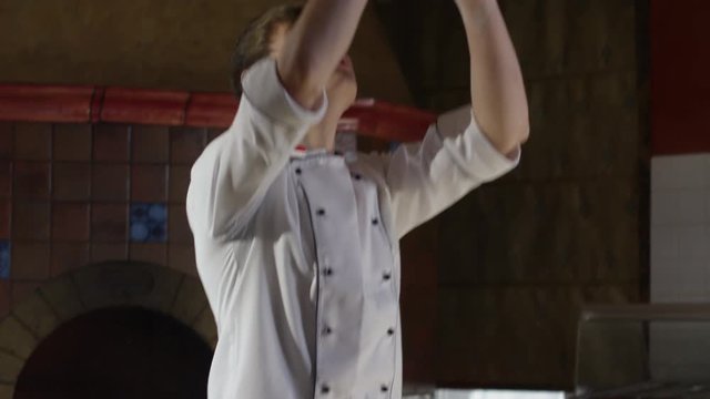 Slow motion shot of young pizzaiolo spinning and tossing pizza dough in restaurant kitchen