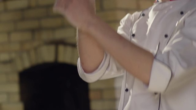 Slow motion of young pizza maker spinning disk of dough on fingertips, turning over head and tossing while working in kitchen