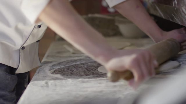 Tilt up of young pizza maker rolling dough on table in the kitchen in slow motion