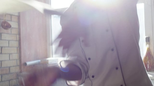 Closeup of pizzaiolo spinning pizza dough and throwing it in the air in sunny restaurant kitchen. Slow motion footage