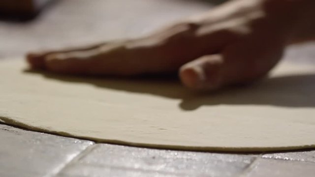 Closeup shot of male hands pressing and turning pizza dough on floury table 