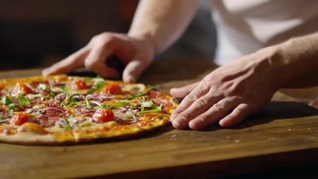 Tracking shot of male hands sliding freshly baked delicious pizza from wooden board to serving plate