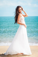 Fototapeta na wymiar Fashion bride walking down the sea coast in a white dress. Beautiful girl walks barefoot down the beach.