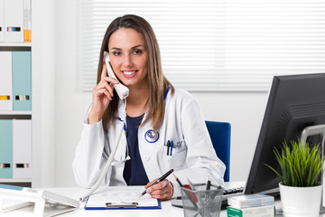 Smiling female Doctor sat at desk with telephone to ear