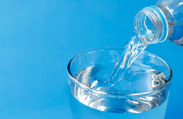 Pouring water into glass on blue background