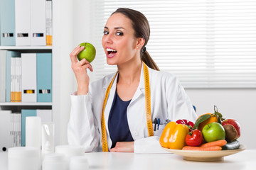 Smiling Female nutritionist eating a Green Apple in her office