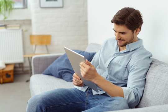 mann sitzt auf dem sofa und schaut auf sein tablet