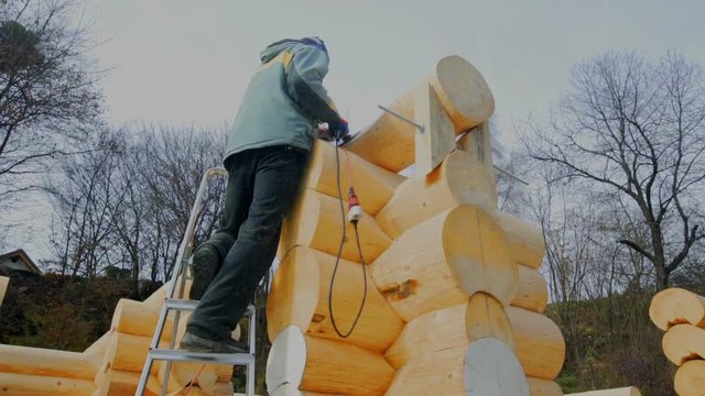 A young man is standing on top of the ladder and he is chiselling wooden and making sure that it is flat and shiny.
