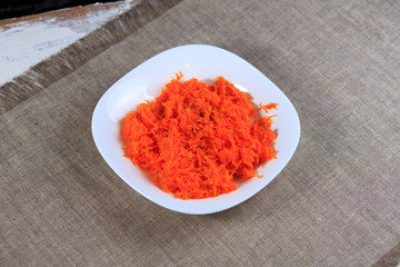 Red boiled carrots on a plate on a gray background among products