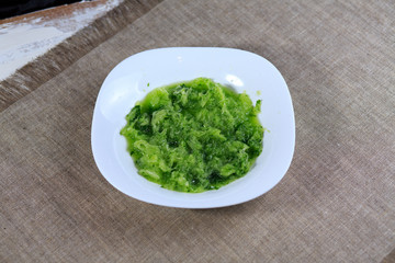 The cucumber grated. Porridge from a fresh green cucumber on a plate on a gray background.