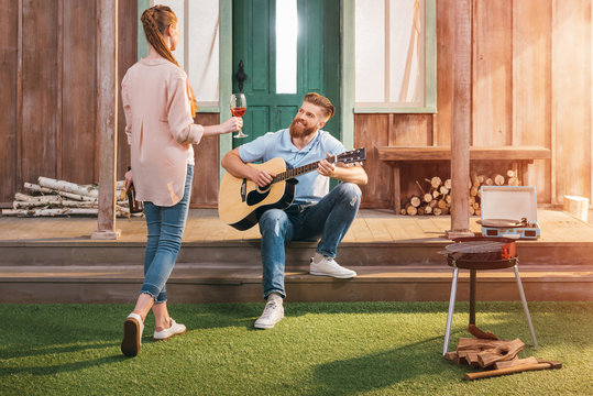 man and woman resting on porch, man playing on guitar
