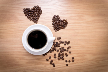 Hot cup of espresso and heart shape made from coffee beans on wooden surface.